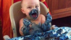 Baby in highchair smeared with blue cake frostong
