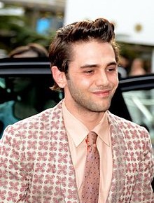 Photo of filmmaker Xavier Dolan, white young man with brown hair, clean shaven, pink patterned suit and tie