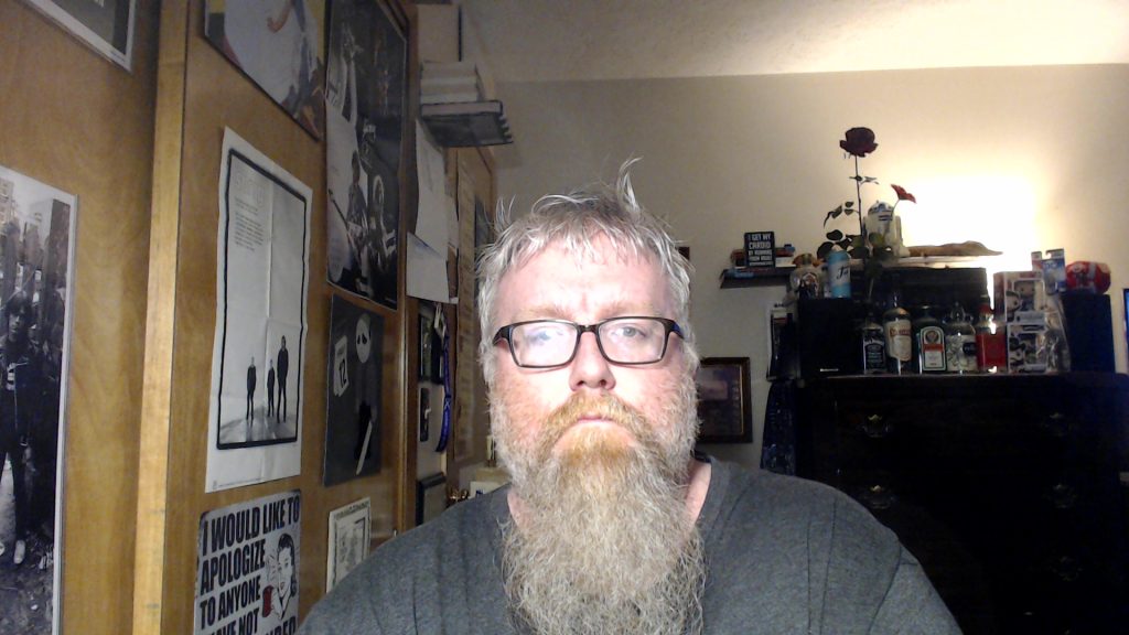 Middle aged white man with a beard standing in a bedroom with posters on the walls
