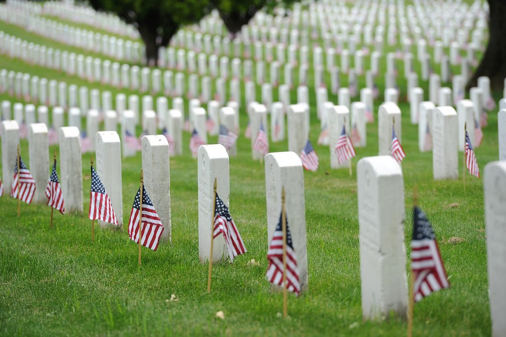 Military cemetery with flags next to rows of white tombstones. 