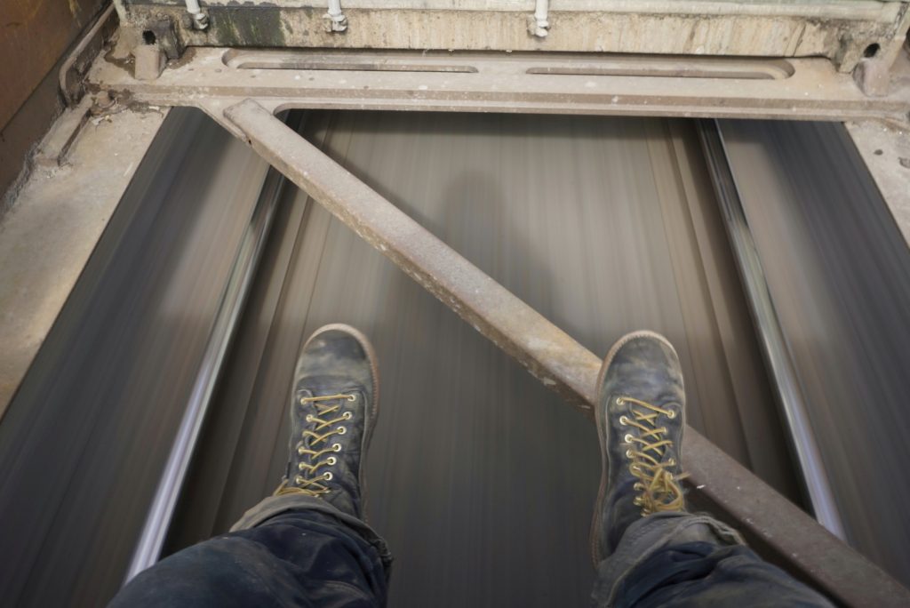 Man's laced up boots in front of part of a moving truck. 