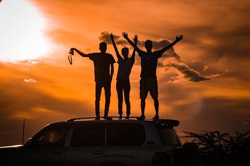 Three people of indiscriminate race standing atop a van in an orange sunset.