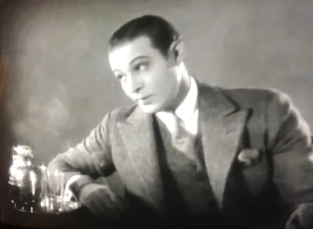 Attractive young white male 1940s movie star, slicked back dark hair and in a suit next to a tumbler of booze. 