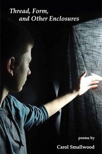 White woman with short dark hair looks out through a curtain towards light outside in a dark room. 