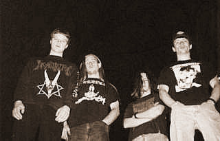 Group of young white guys posing for a black and white photo. They all have tee shirts and jeans, one has a pentagram and the others have different designs. One has a baseball cap.