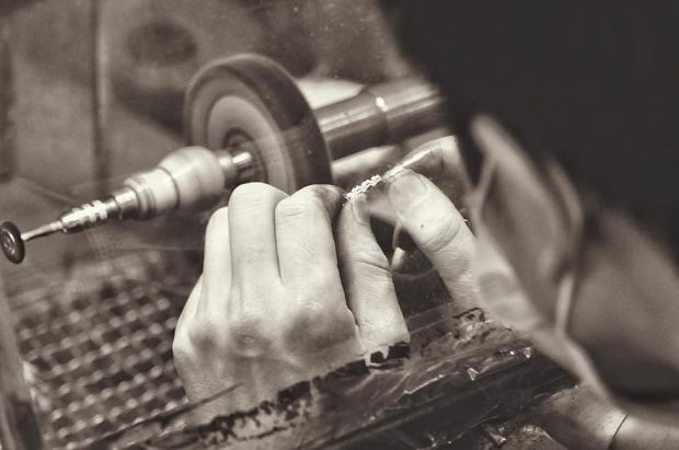 Person holds beads on a bracelet over a refining tool to polish them, in a black and white sepia photo.