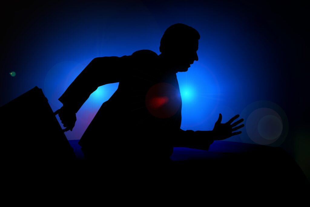 Nondescript shadowy male figure running against a blue and black background carrying a briefcase in his right hand. 
