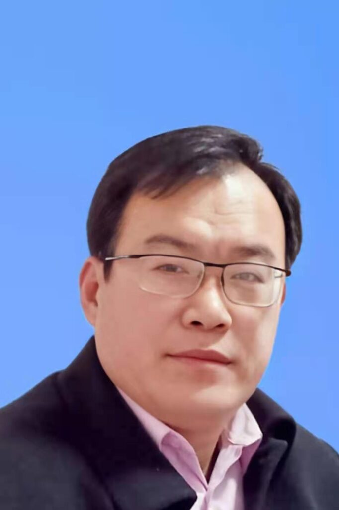 Asian man with glasses and short brown combed hair, wearing a black coat.