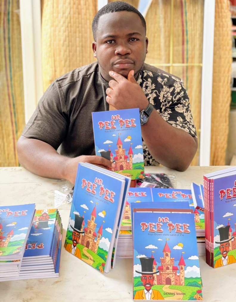 Young Black man sitting at a table in front of a pile of Mr. Pee Pee books. 