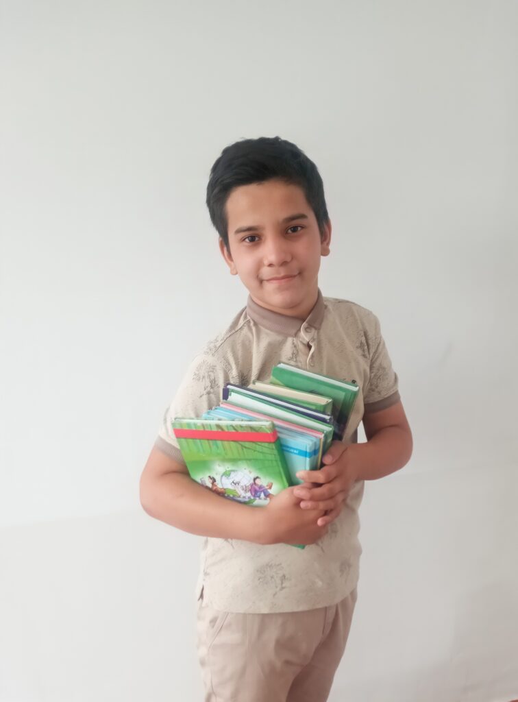 Boy with light skin and short brown hair carrying an armful of books