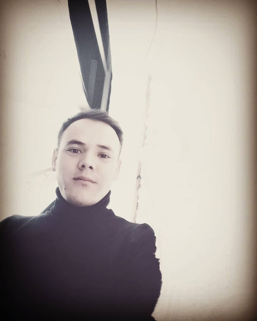 Young Central Asian man in a black turtleneck with short hair and brown eyes.