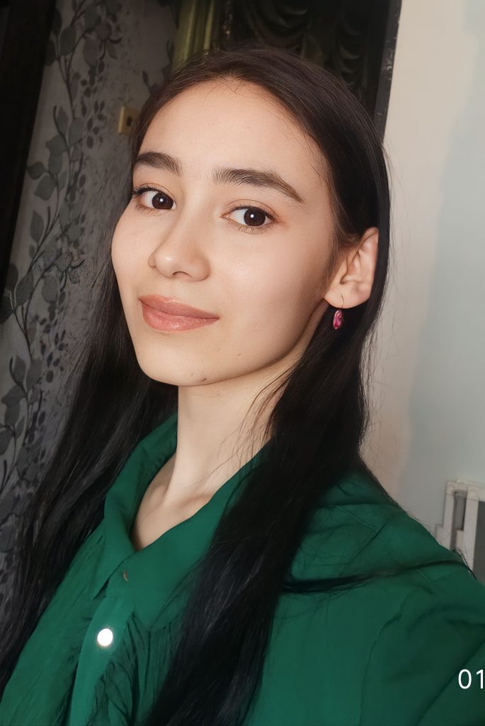 Young Central Asian woman with black hair and brown eyes and a dark green collared silk top. 