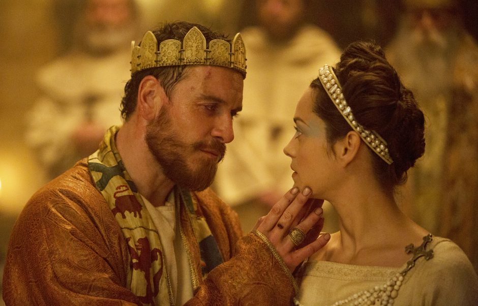 Macbeth and his wife. A man wearing a king's crown and a robe and scarf tenderly touches the chin of a woman with a headband and a dress. 