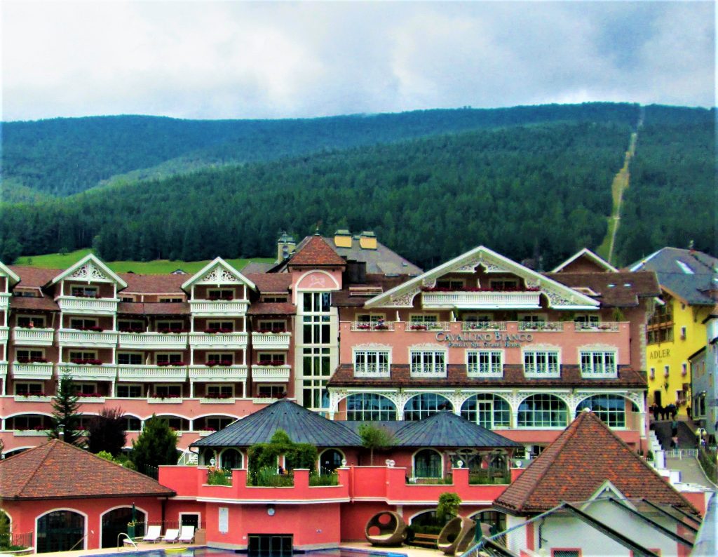 Apartment buildings with sloping roofs in peach and brown in front of large forested rolling hills