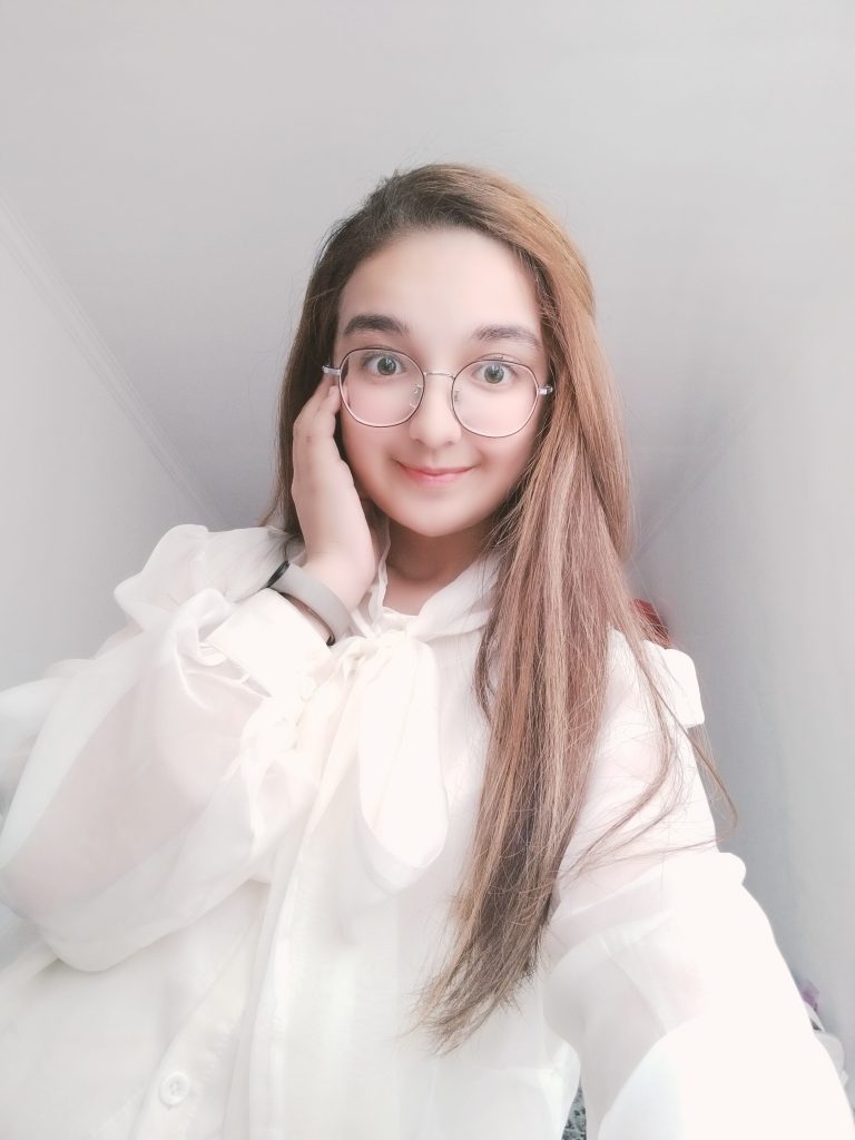 Central Asian teen girl with long light brown hair, reading glasses, and a fluffy white blouse with a bow in the front. 