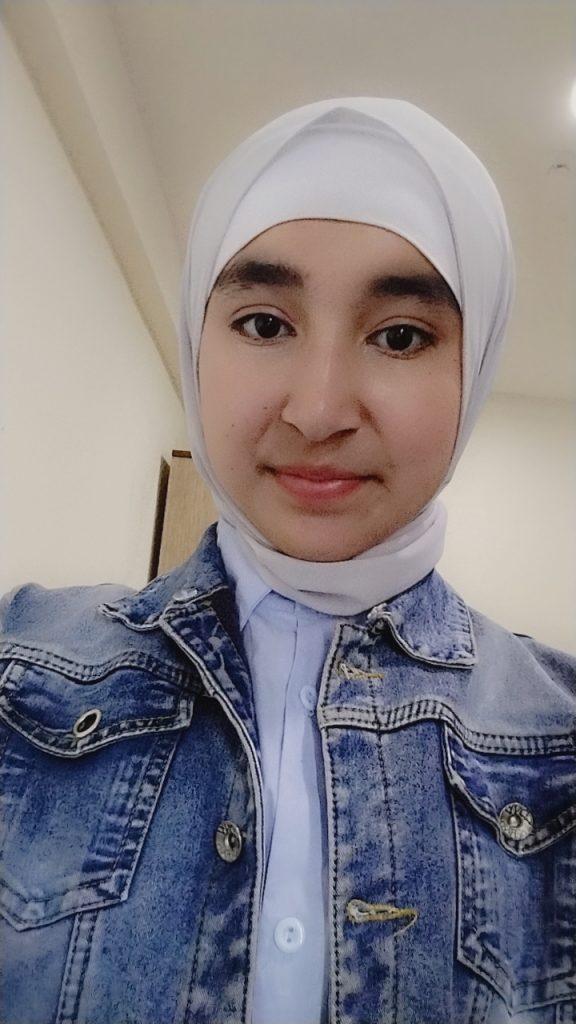 Young Central Asian woman with a headscarf and brown eyes. She's got a jean jacket over a blue collared shirt. 