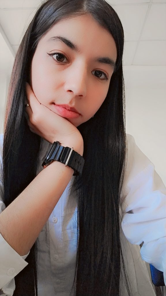 Young Central Asian woman with straight black hair, brown eyes, and her head resting on her hand. She's got a wristwatch on and is in a white buttoned top. 