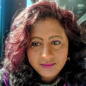 South Asian woman's face. She has reddish curly hair, brown eyes, and pink lipstick. 