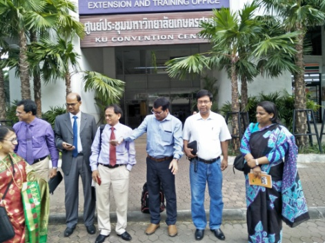Group of middle aged adults in front of a school building with signs in Thai with palm trees 