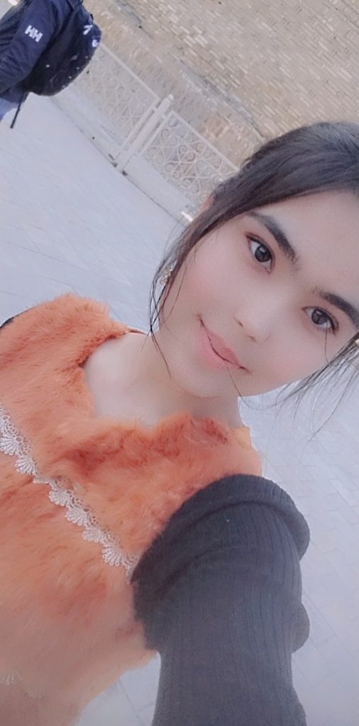 Young Central Asian teen girl with straight dark hair, brown eyes, and an orange top, pictured at a diagonal.