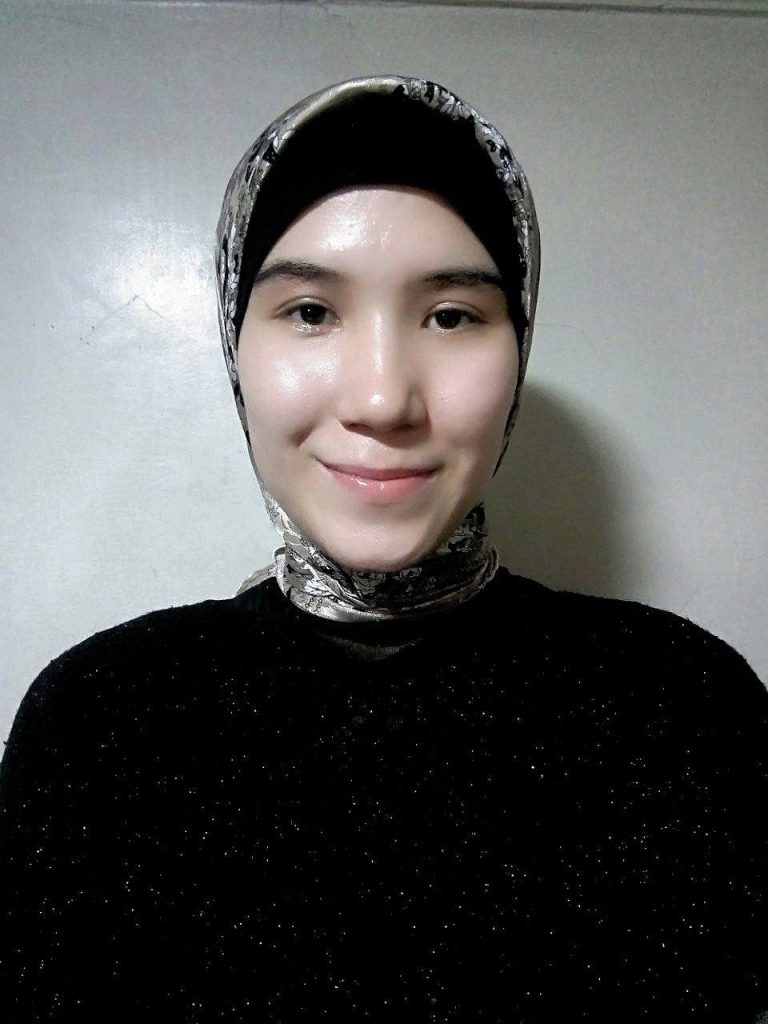 Young Central Asian woman with a headscarf over her hair. She's got a black sparkly sweater. 