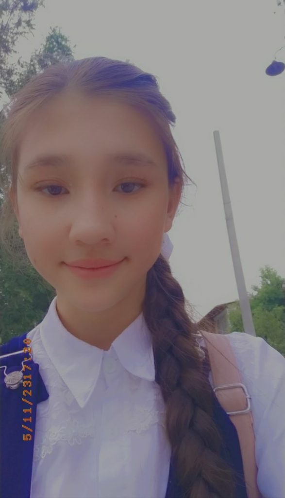 Young Central Asian girl with dark hair up in a braid and a white lacy collared shirt and a backpack. 