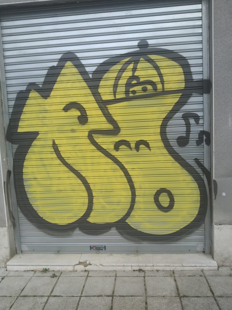 Two yellow figures in graffiti, outlined in black, on a metal door in the city.