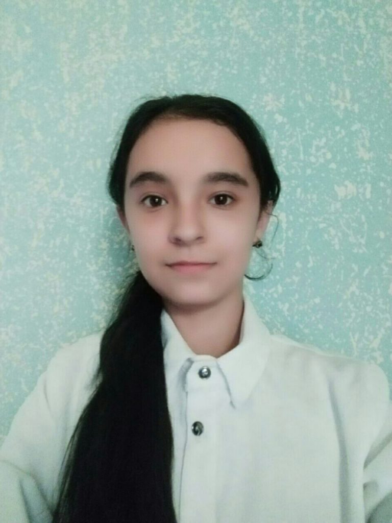 Young Central Asian teen girl with black hair up in a ponytail and a white collared shirt. 