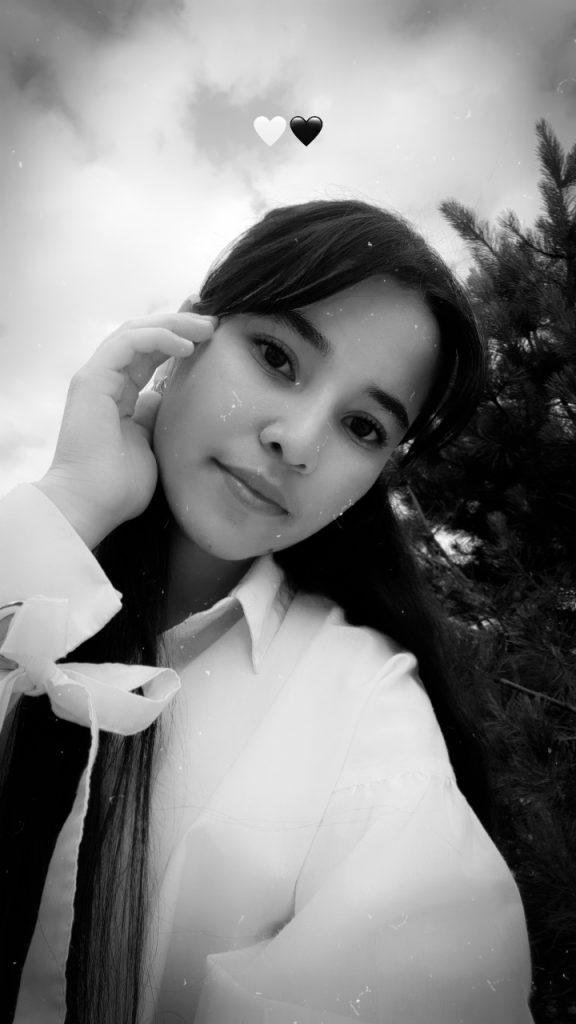 Young Central Asian teen girl with long black hair and brown eyes. She's in a white collared blouse and leaning to the right. She's outside by a tree. 