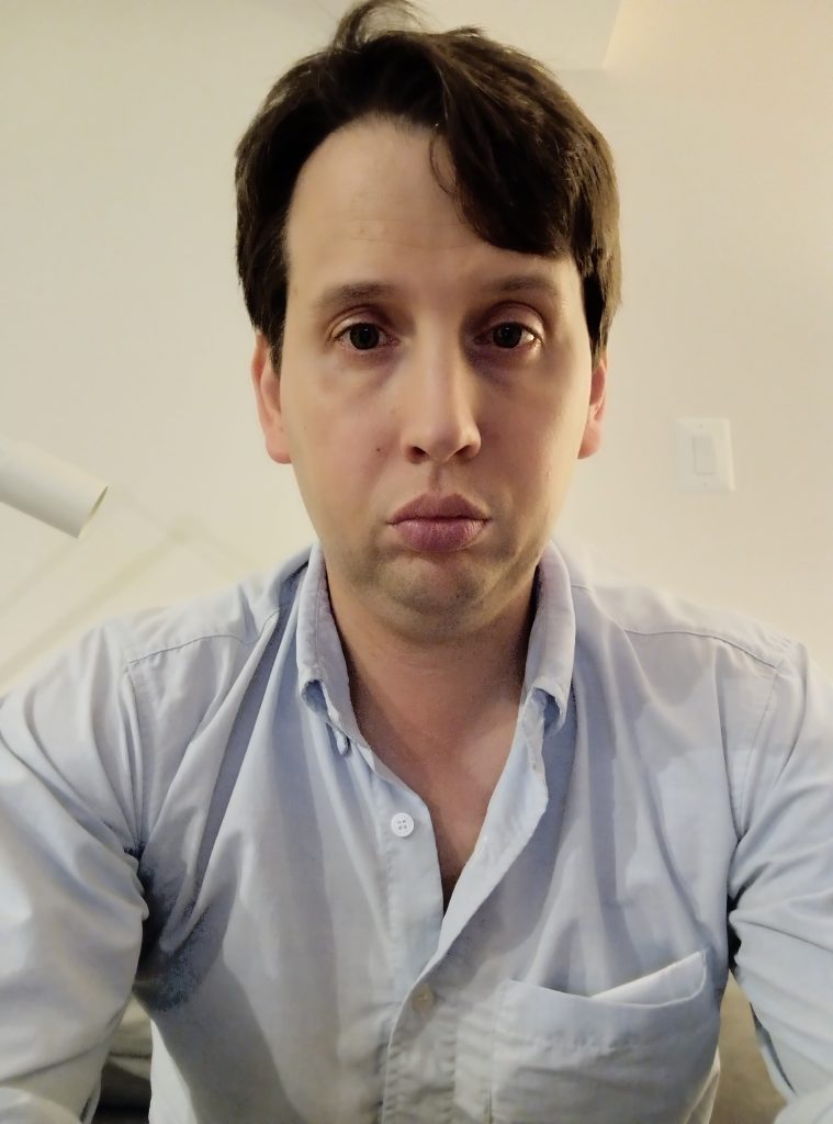 Young adult white man with brown hair and eyes and a light blue collared shirt. 