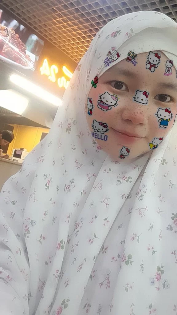 Young Central Asian woman with a white lacy headscarf with flowers on her outfit and smiling Hello Kitty icons on her face.
