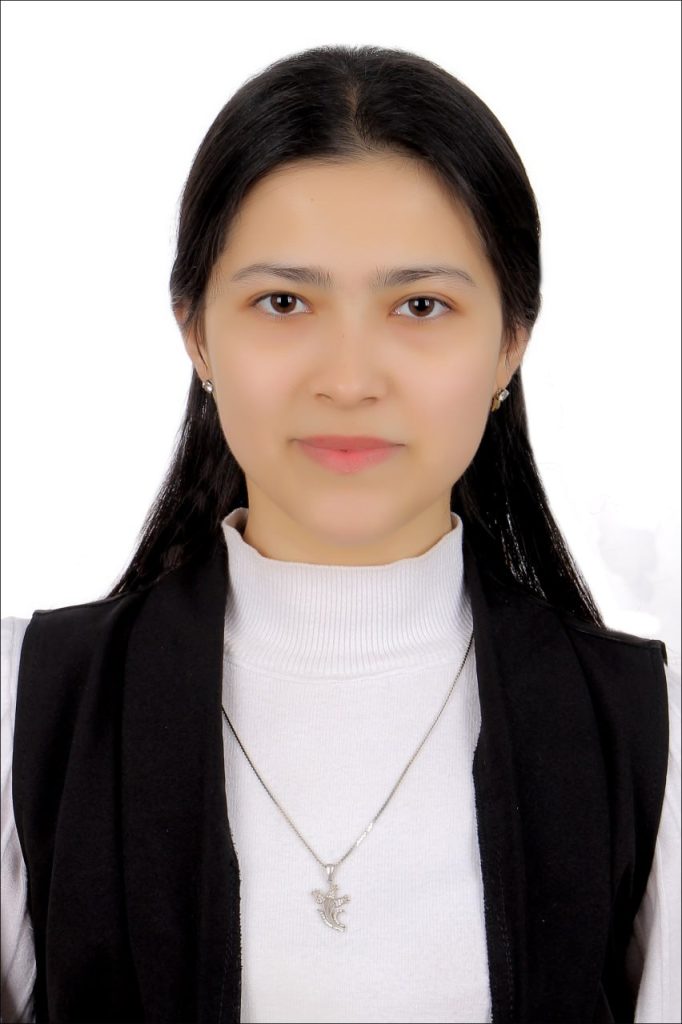 Young Central Asian teen girl with dark black hair and brown eyes an dearrings and a black vest over a white collared shirt and necklace. 