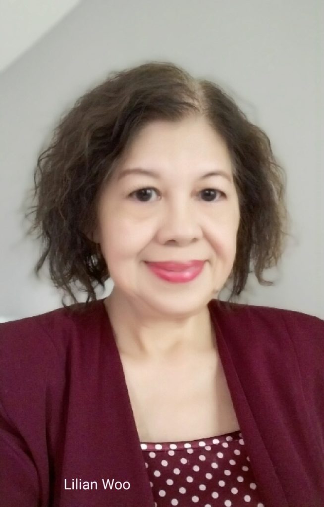 Middle aged East Asian woman with light skin, brown curly hair and a burgundy jacket and white polka dotted blouse. 
