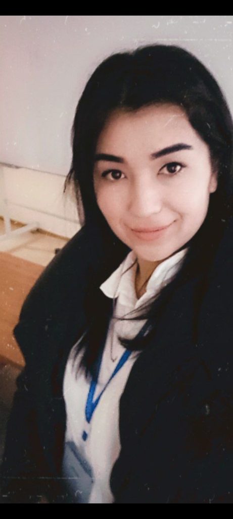 Young Central Asian woman with straight brown hair, brown eyes, and a black jacket and white collared shirt. 