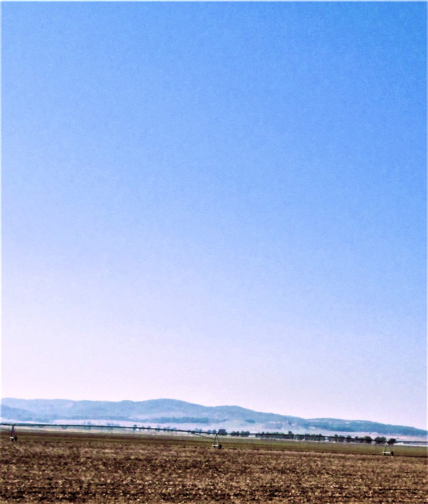 Large dark and light blue sky, mountains in the distance, brown fields below. 