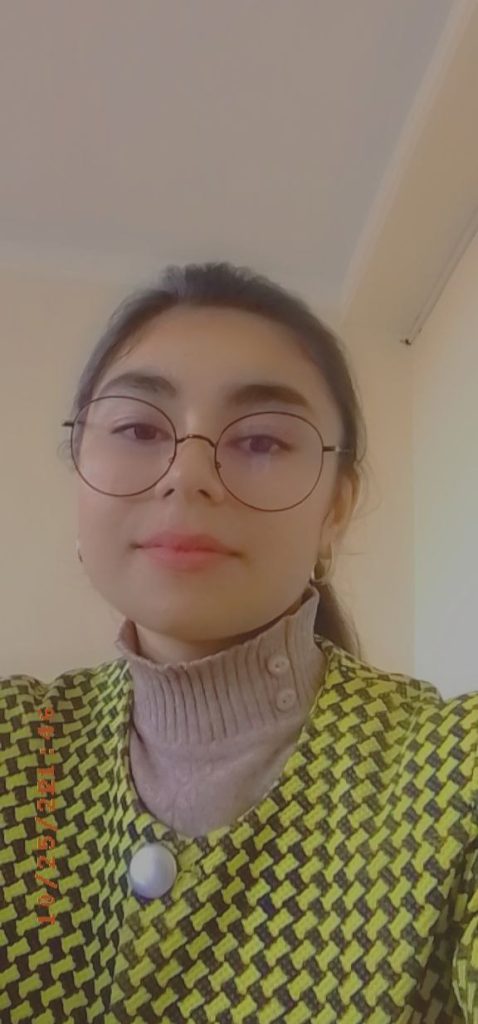 Young teen Central Asian girl with reading glasses, a pink turtleneck sweater, and a black and yellow checkered coat. 