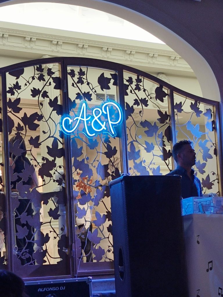 Wedding DJ in front of a large speaker in the evening in front of a metal wall with carved leaves and the initials "A and P." 