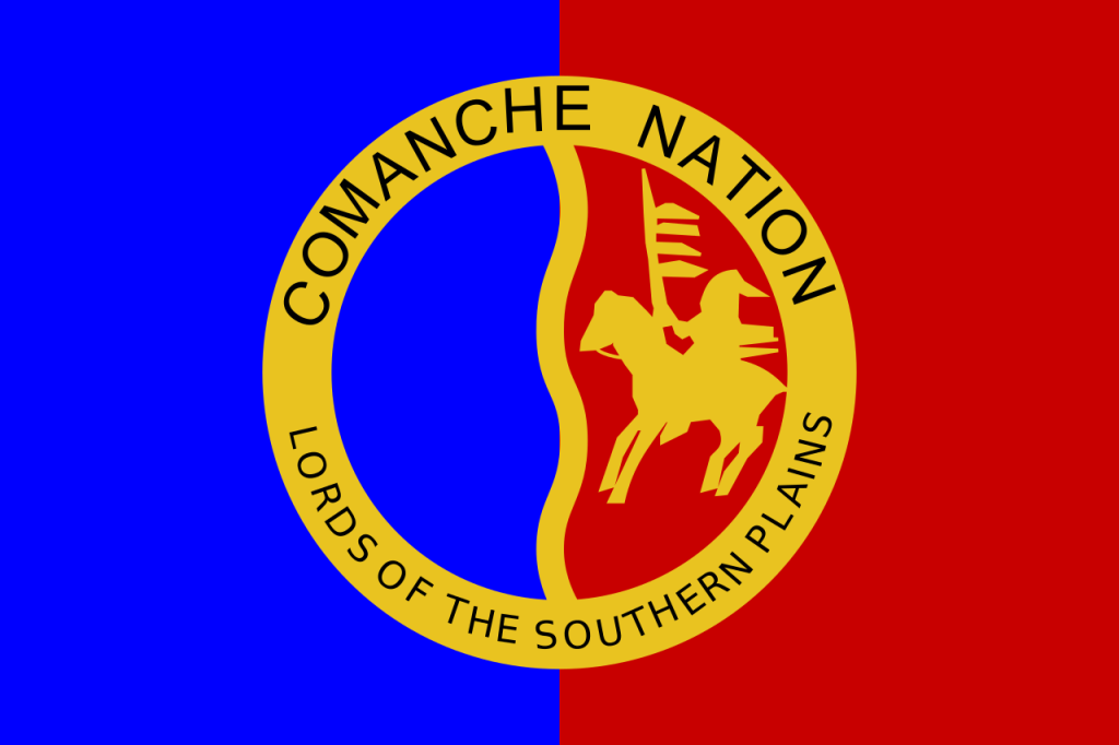 Red and blue flag with a yellow circular seal and a yellow person on horseback in the middle. Black text on the seal reads "Comanche Nation, Lords of the Southern Plains." 