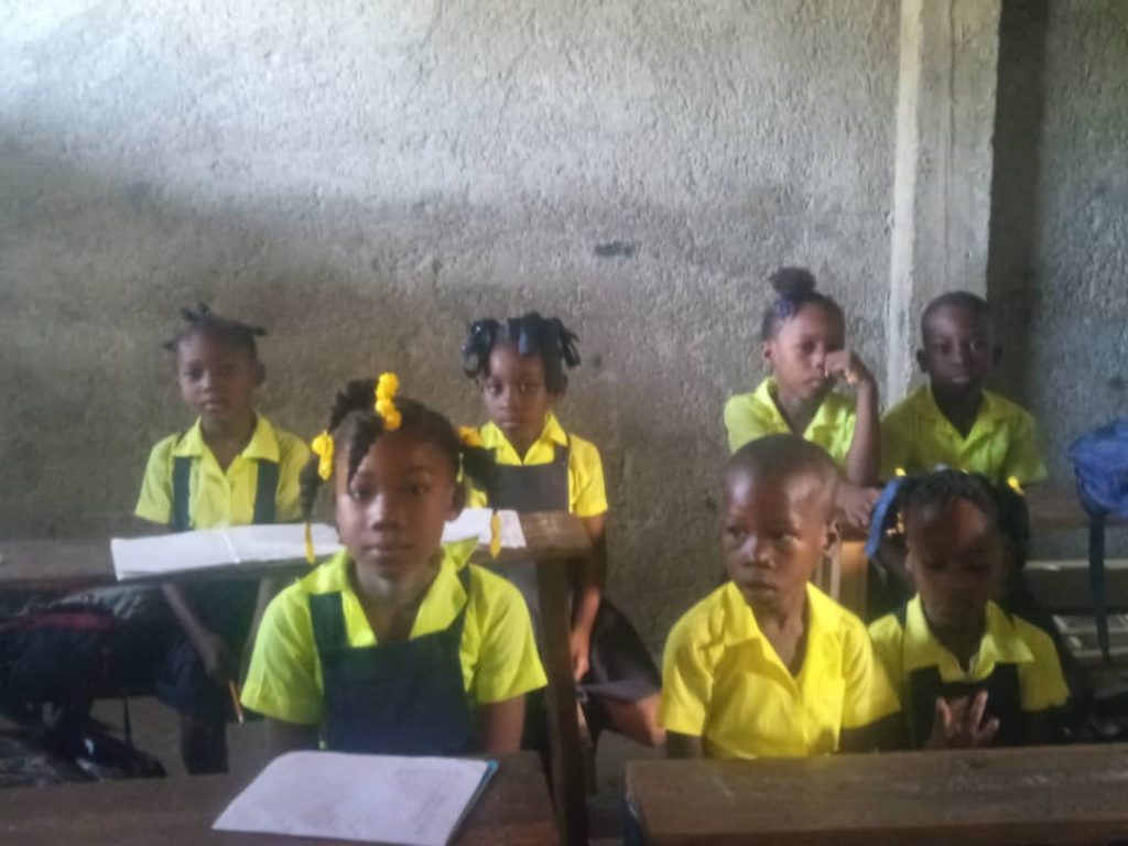 Smaller group of children at desks, some have paper and pencils in front of them. 