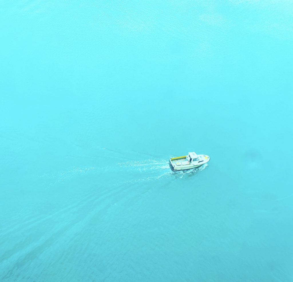 Small boat with a small wake on light blue water. 