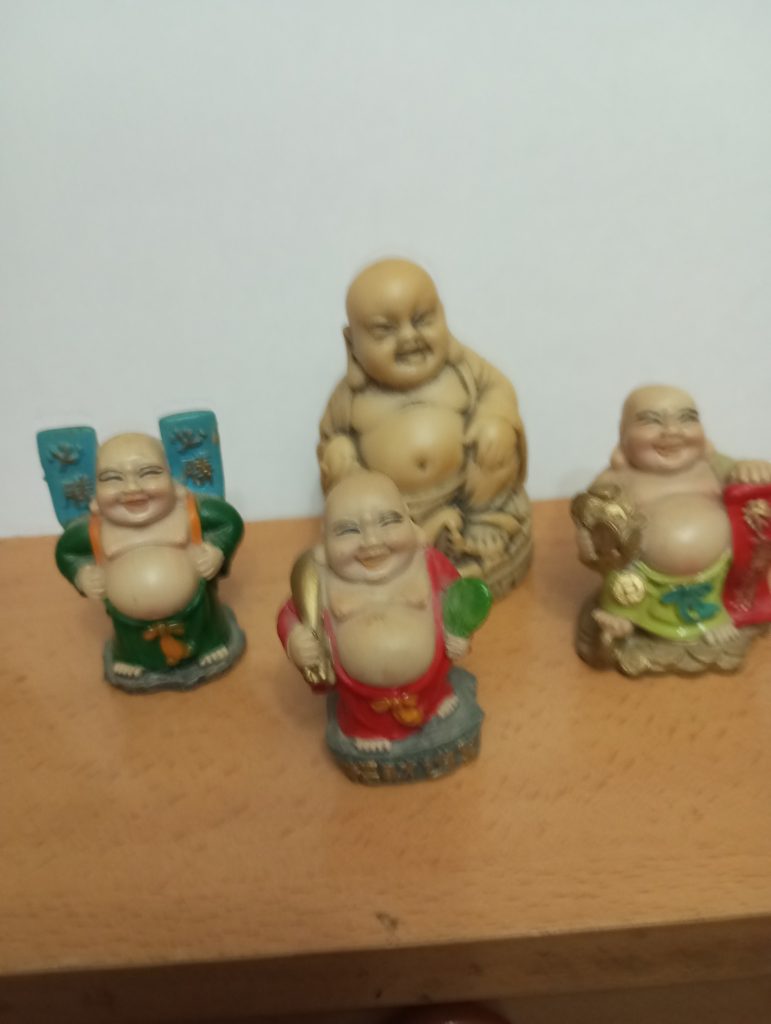 Slightly blurred image of four Buddhas, one in the background that's larger with a solid color. 