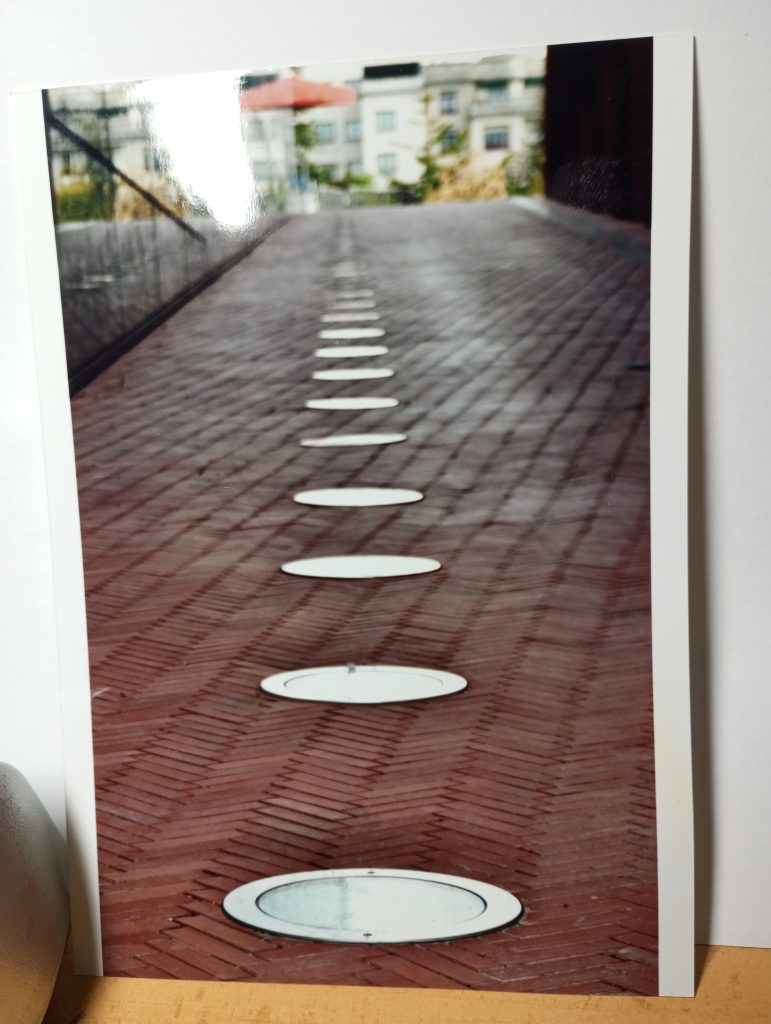 Brick patio with circular figures on the road and buildings in the distance. 