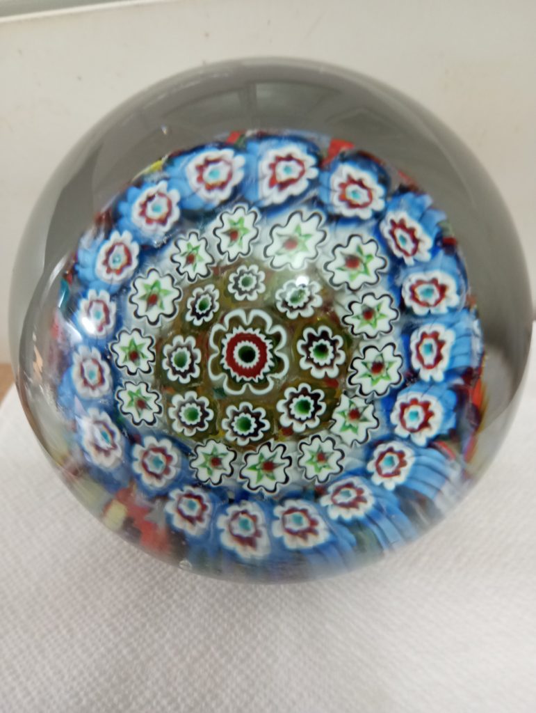 Glass with a painted mandala, red, white, blue and green flowers in concentric circles. 