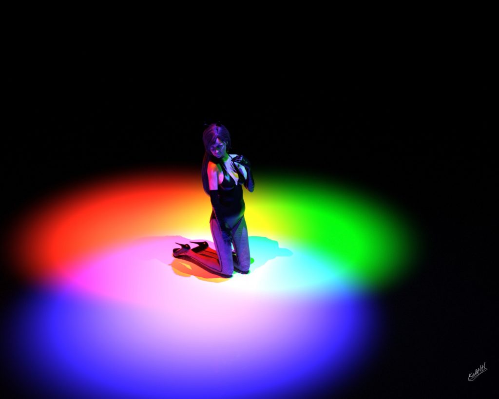 Woman of undetermined age and skin tone kneeling and looking to the ground under spotlights of green, red, and blue. Everywhere else is pitch black.
