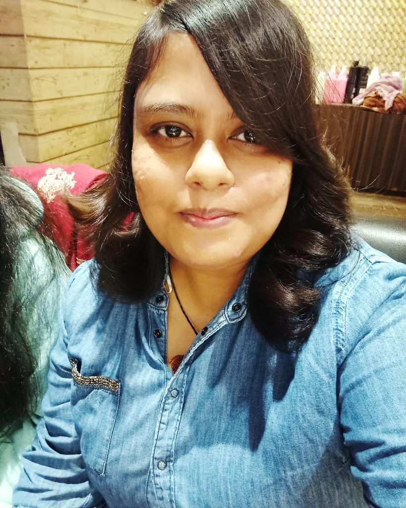 Young South Asian woman with dark hair and brown eyes and a blue jean jacket and necklace. 