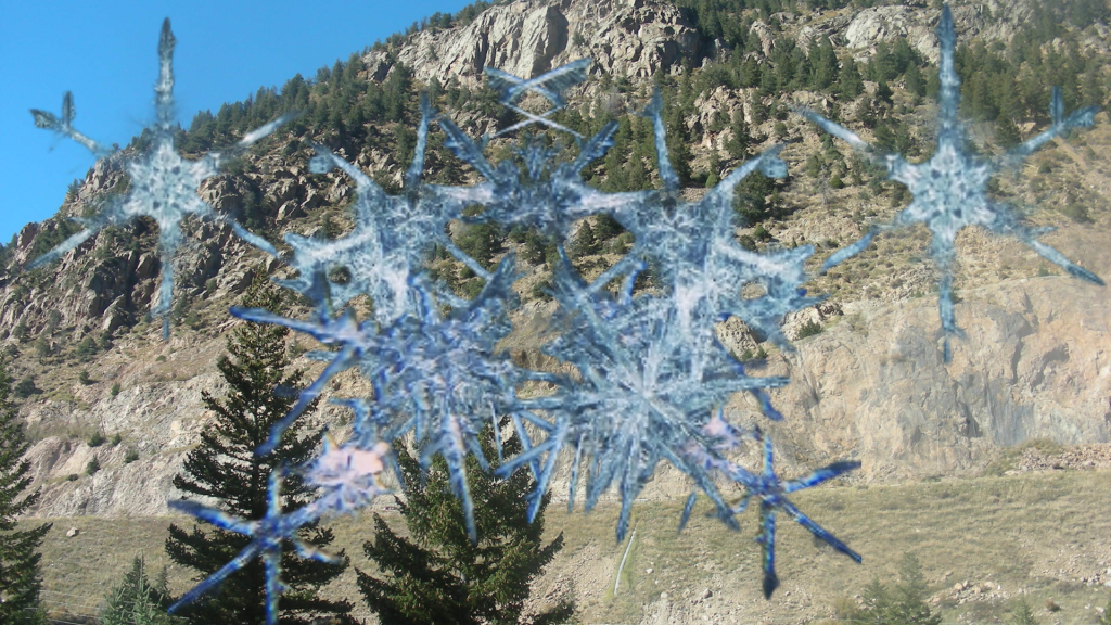 Snowflakes in front of a tree-lined and rocky mountain vista. 