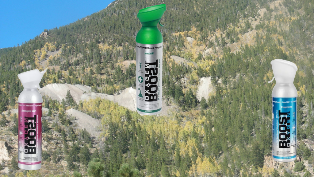 Mountain vista with trees and rocks in the background and three differently colored oxygen canisters in the foreground. 