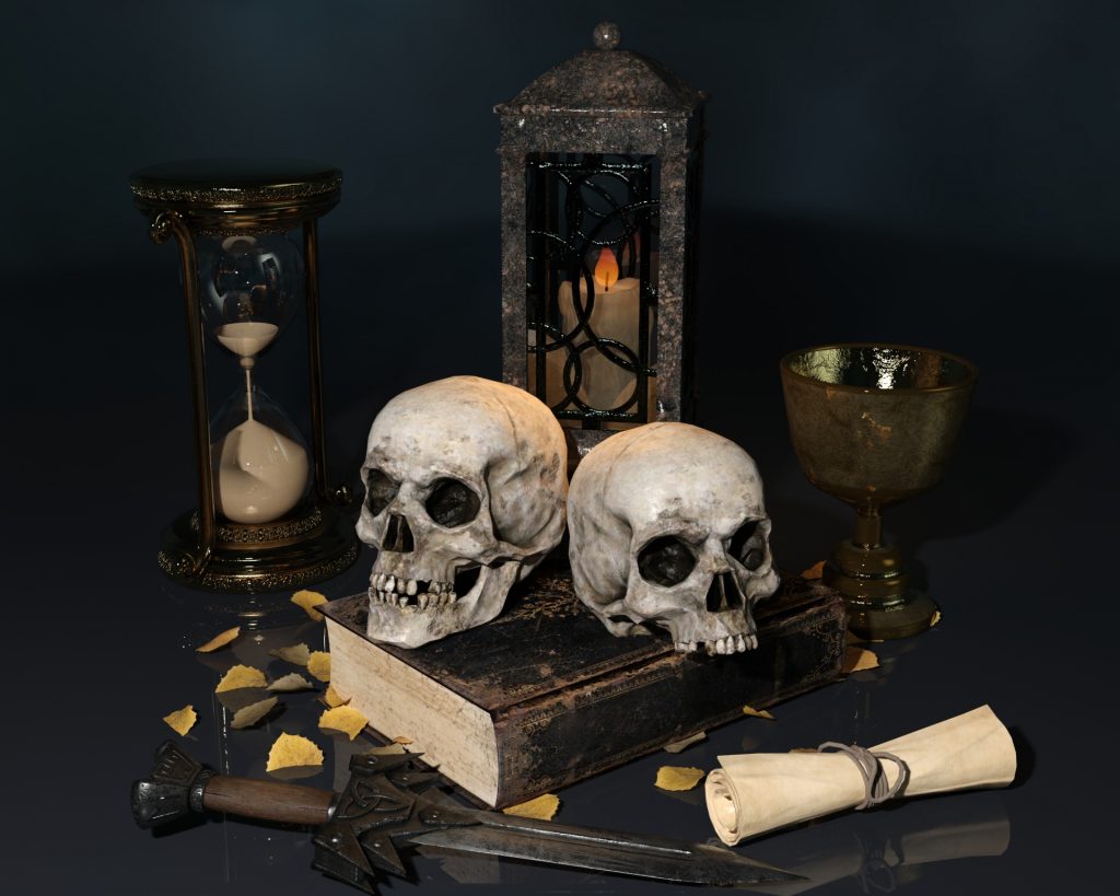 Vanitas style composition with skulls, old books, a rolled up paper, candles, leaves, and an hourglass. 