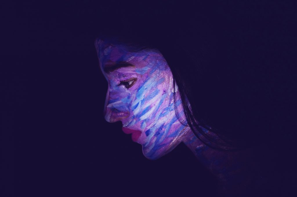 Woman with a painted blue and white and purple face in outline on a dark blue background. 