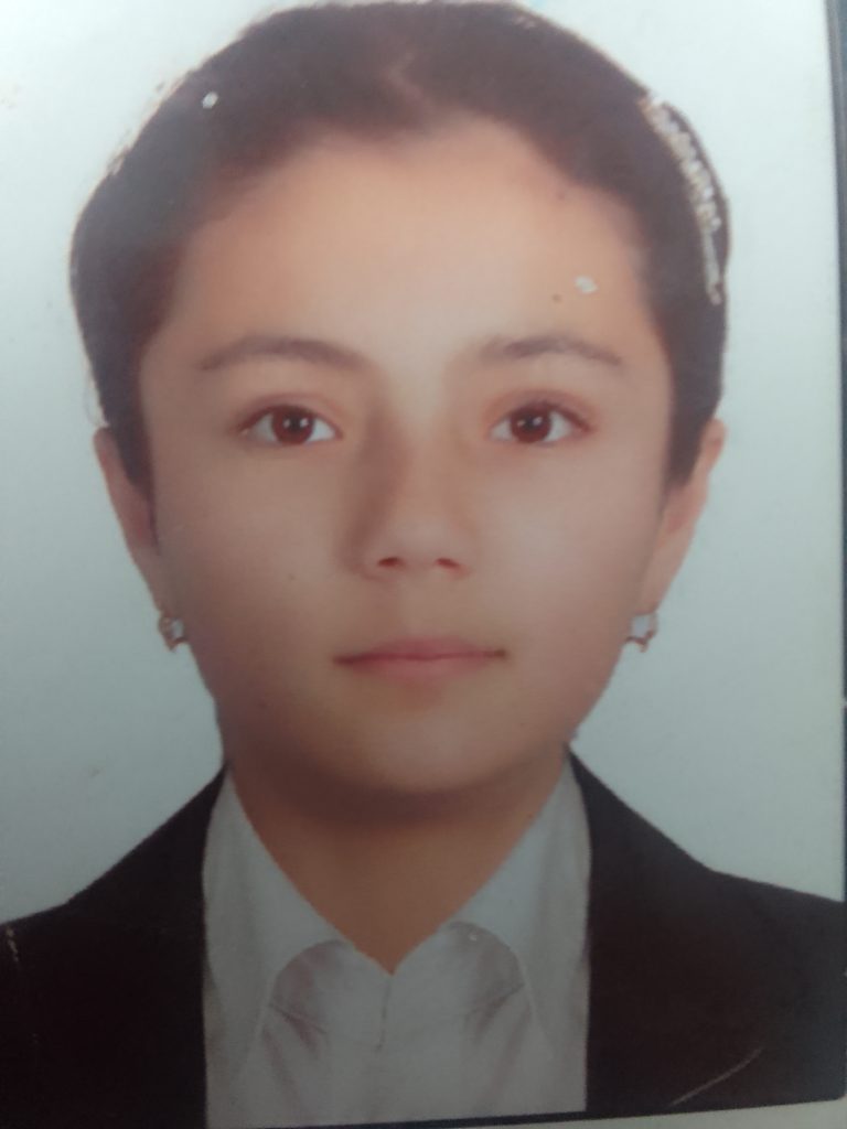 Young Central Asian teen girl with brown eyes and brown hair behind her head, earrings and a black coat over a white collared shirt. 